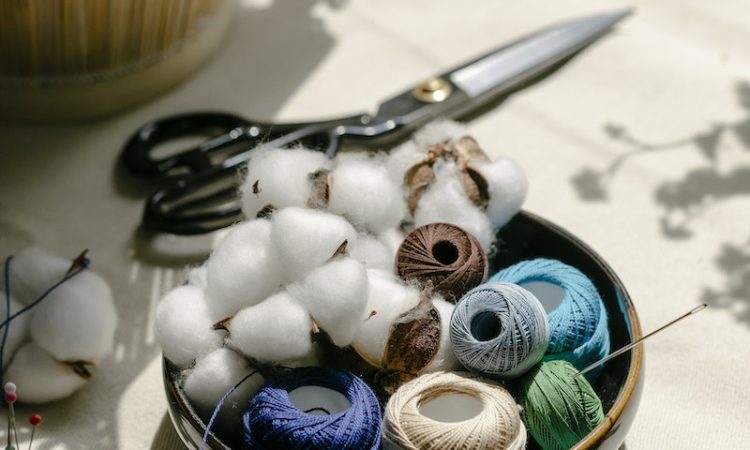 Thread bobbins with scissors and needles placed on table in atelier